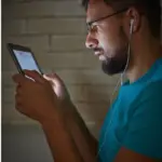 Guy reading something on a tablet. He has a headphone in his ears